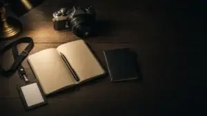 Novinářský press pass, fotoaparát, zápisník a pas na tmavém stole ve světle lampy