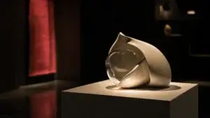 Bílý sokl s designovým keramickým objektem nasvícený bodovým světlem v tmavém výstavním stánku